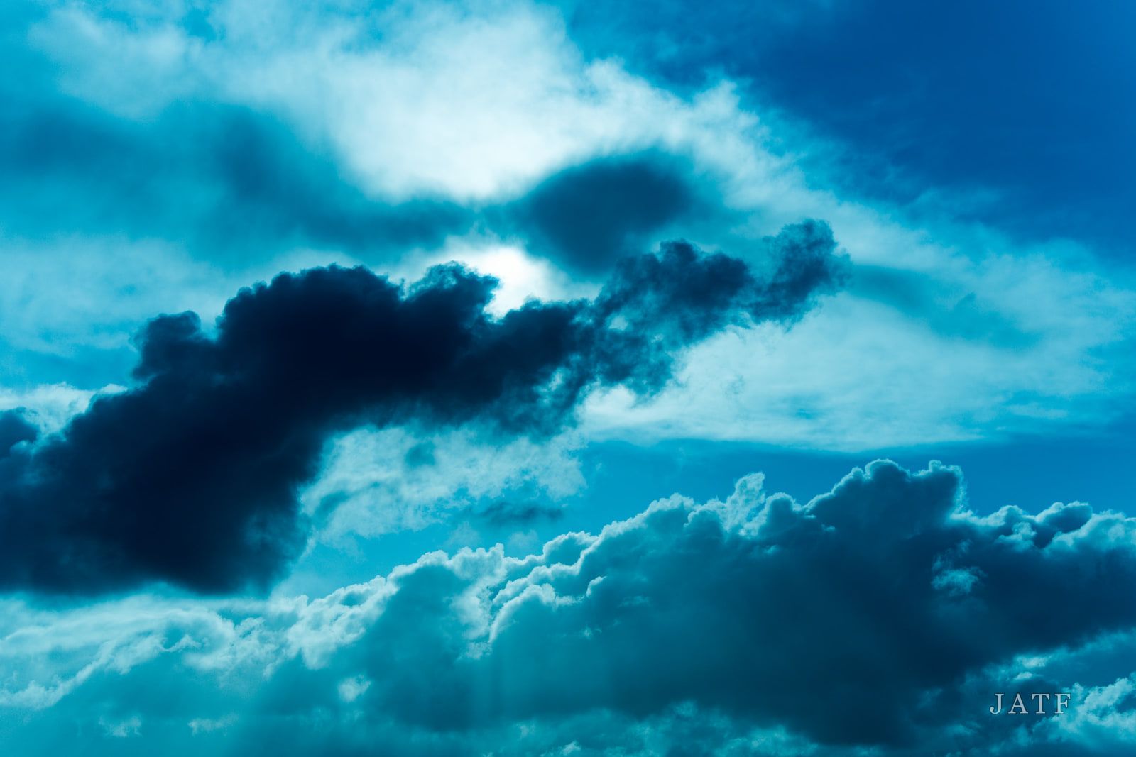 Dark storm cloud breaking apart against deep blue sky, lit from behind