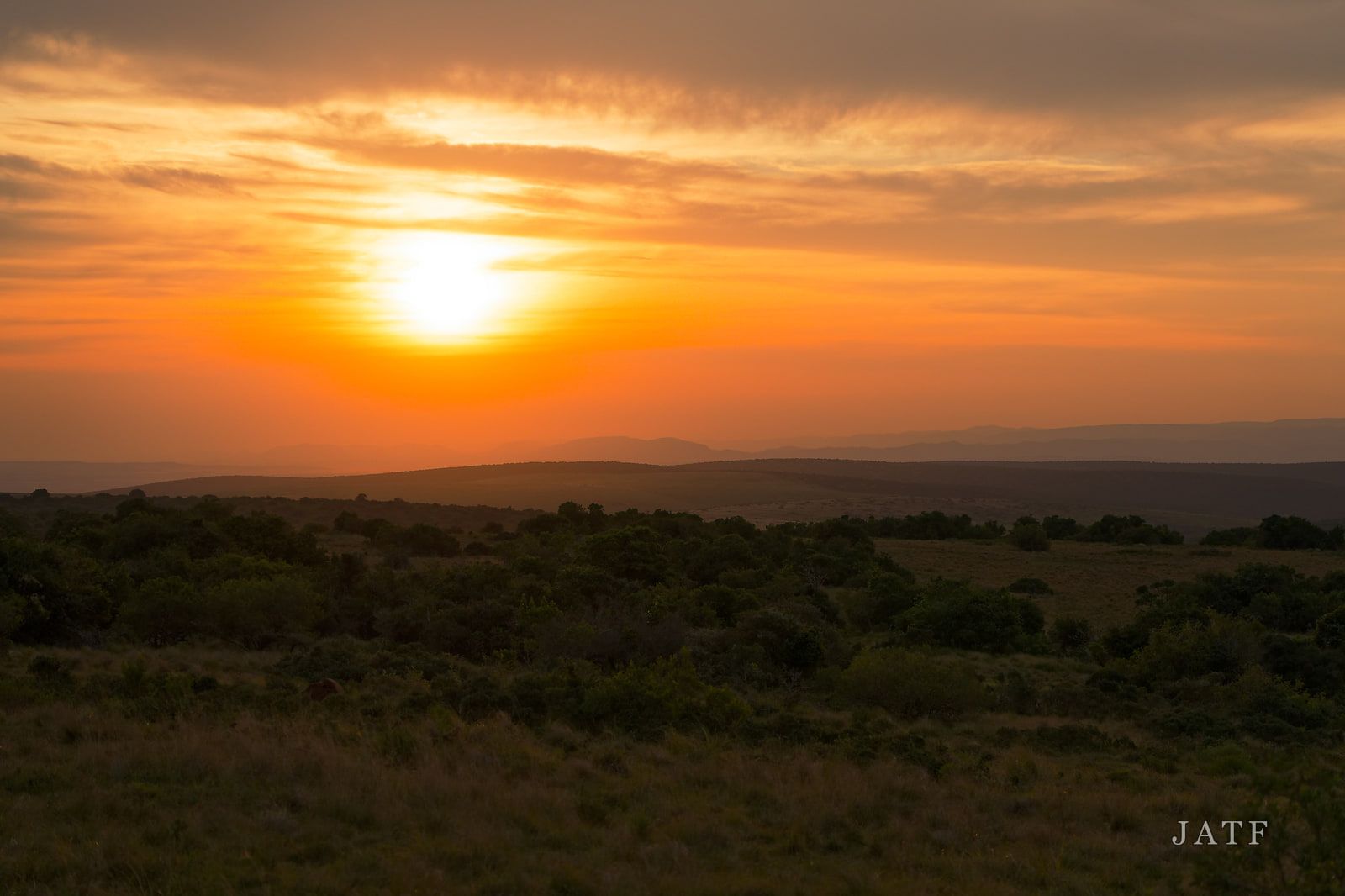 Sun setting through banded cloud over rolling bush country